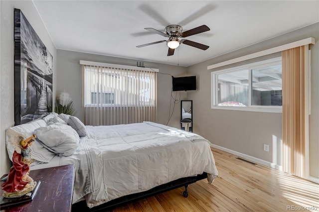 bedroom with a ceiling fan, wood finished floors, visible vents, and baseboards