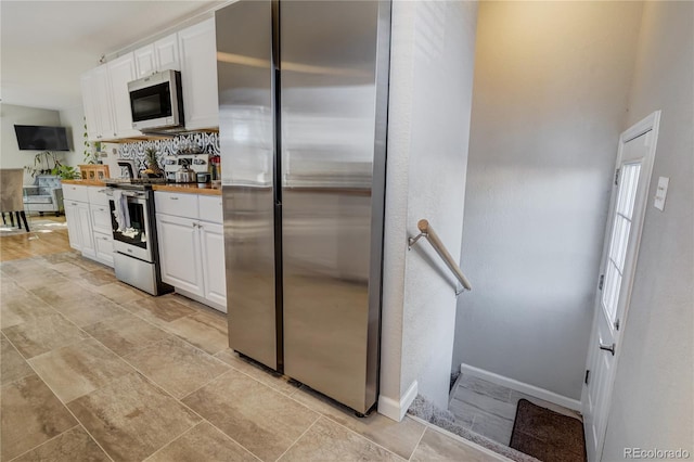 kitchen with stainless steel appliances, white cabinets, wooden counters, and baseboards