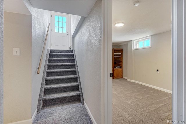 stairway featuring a textured wall, carpet floors, and baseboards