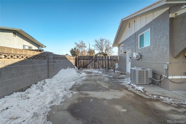 yard covered in snow featuring a gate, fence, and central AC unit