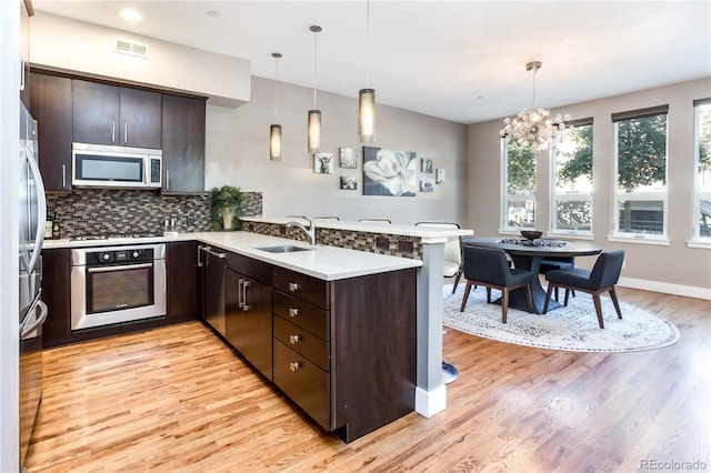 kitchen featuring appliances with stainless steel finishes, sink, dark brown cabinets, kitchen peninsula, and pendant lighting