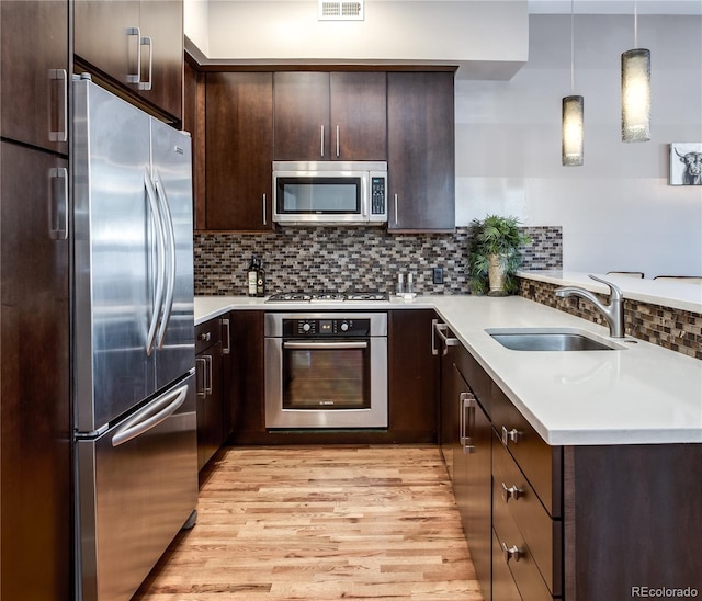 kitchen featuring hanging light fixtures, light hardwood / wood-style flooring, stainless steel appliances, sink, and tasteful backsplash