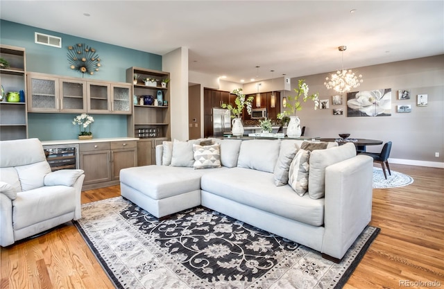 living room featuring light hardwood / wood-style flooring, an inviting chandelier, and beverage cooler