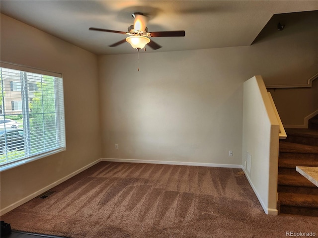 carpeted empty room featuring a ceiling fan, visible vents, stairway, and baseboards