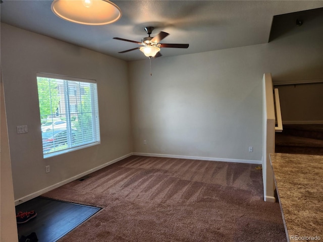 interior space featuring baseboards, visible vents, dark carpet, and a ceiling fan