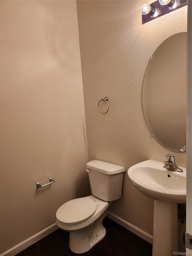 bathroom with a textured wall, toilet, and baseboards