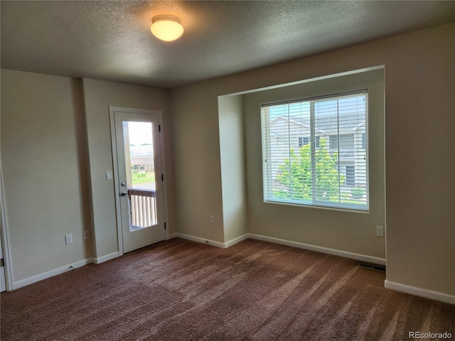 unfurnished room featuring a healthy amount of sunlight, baseboards, dark colored carpet, and a textured ceiling