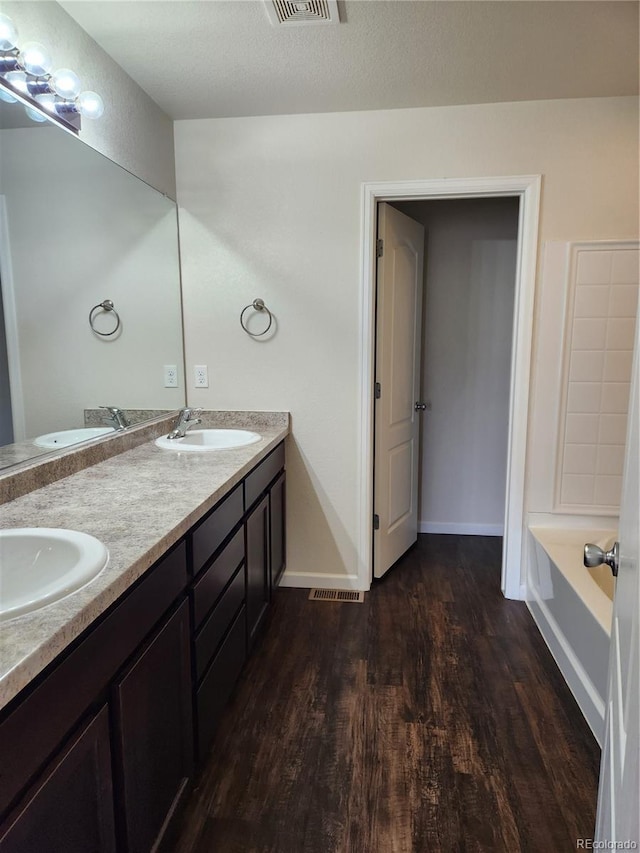 bathroom with wood finished floors, a sink, baseboards, and double vanity