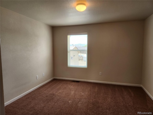 spare room with visible vents, dark carpet, and baseboards