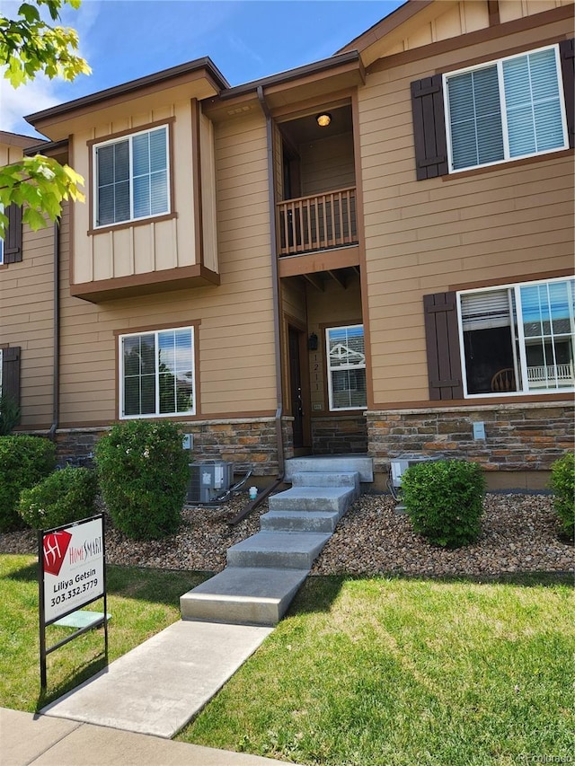 1211 Bistre St, Longmont, CO 80501 - view of front facade with a balcony, stone siding, board and batten siding, central air condition unit, and a front lawn