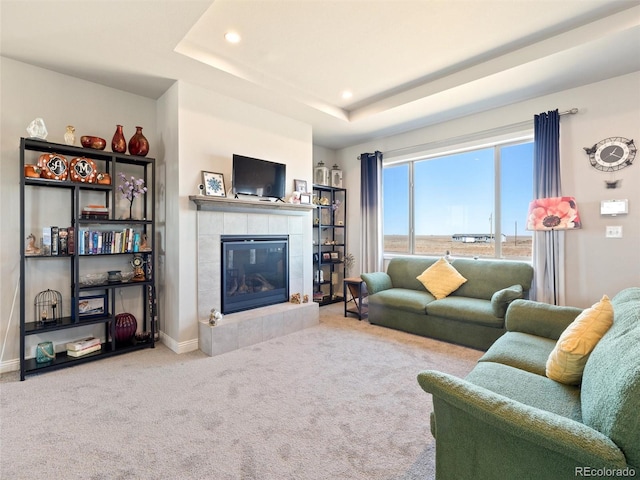 carpeted living area featuring a tile fireplace, a raised ceiling, baseboards, and recessed lighting