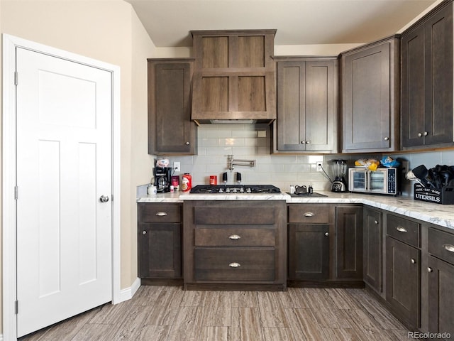 kitchen with stainless steel gas cooktop, wall chimney exhaust hood, dark brown cabinetry, and decorative backsplash