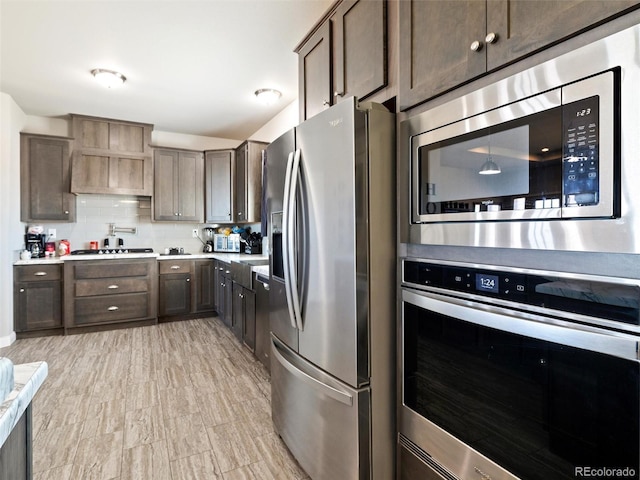 kitchen featuring stainless steel appliances, light countertops, dark brown cabinetry, and decorative backsplash