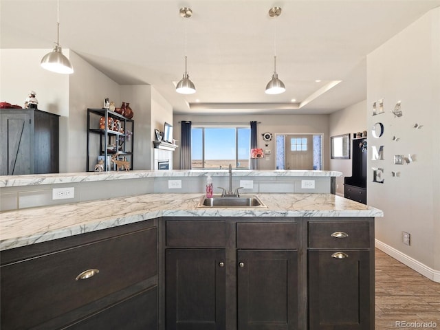 kitchen featuring a tray ceiling, decorative light fixtures, a sink, dark brown cabinets, and light wood-type flooring