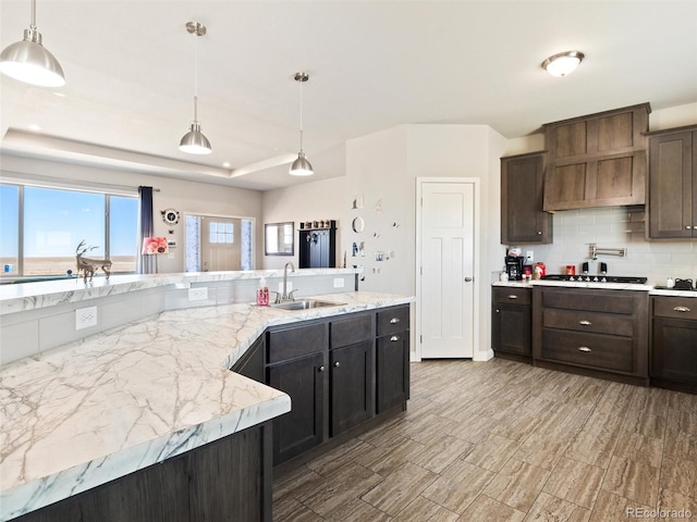 kitchen with dark brown cabinetry, a sink, decorative backsplash, a raised ceiling, and decorative light fixtures