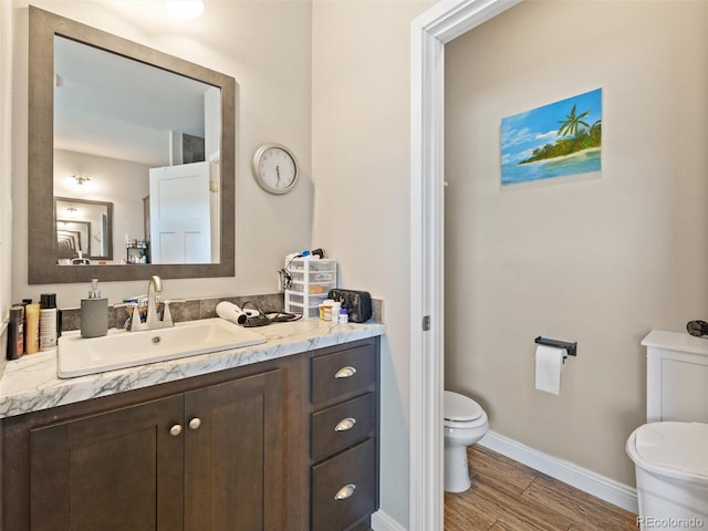 bathroom with toilet, baseboards, wood finished floors, and vanity