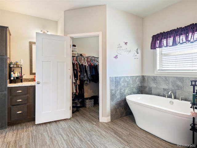 bathroom with a walk in closet, a soaking tub, and tile walls