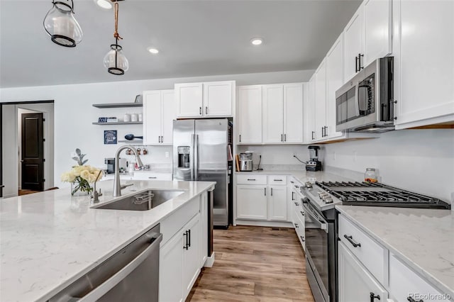 kitchen featuring light stone countertops, appliances with stainless steel finishes, a sink, white cabinetry, and decorative light fixtures