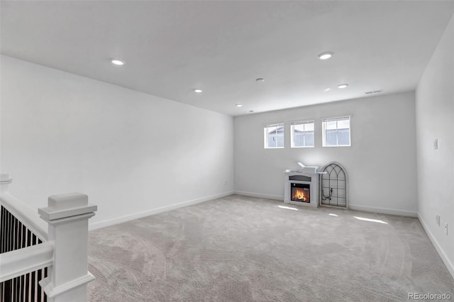 unfurnished living room featuring carpet floors, visible vents, a glass covered fireplace, baseboards, and recessed lighting