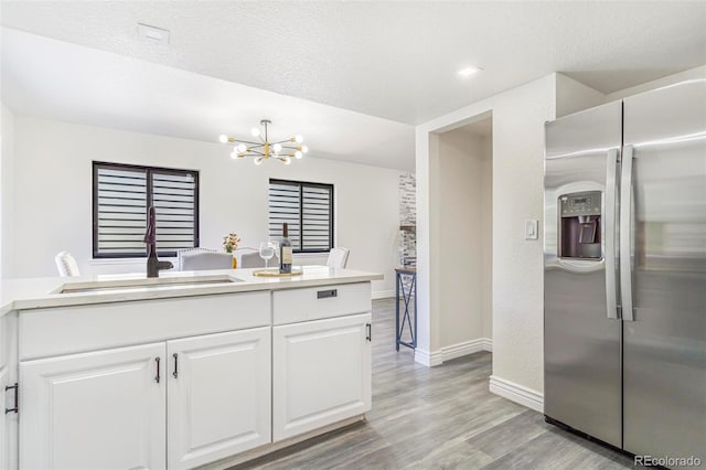 18751 E Mexico Ave, Aurora, CO 80017 - kitchen with stainless steel fridge, a chandelier, white cabinets, light wood finished floors, and light countertops
