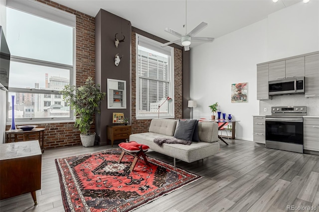 living room with light wood-style flooring, brick wall, a ceiling fan, and a towering ceiling