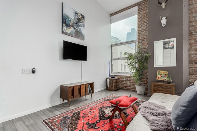 living area with wood finished floors, baseboards, and brick wall