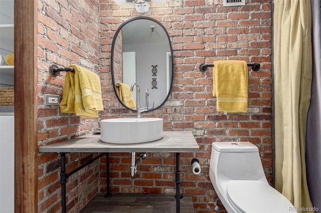 bathroom featuring brick wall, toilet, and a sink