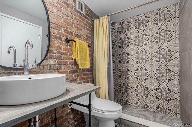 bathroom with visible vents, brick wall, toilet, a tile shower, and a sink