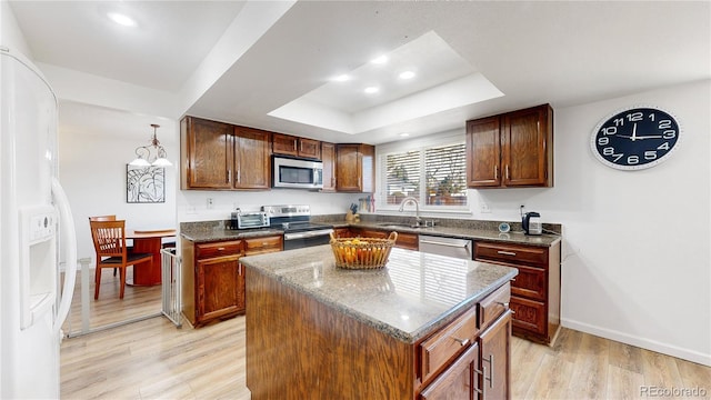 kitchen featuring a center island, sink, stainless steel appliances, a raised ceiling, and light hardwood / wood-style flooring