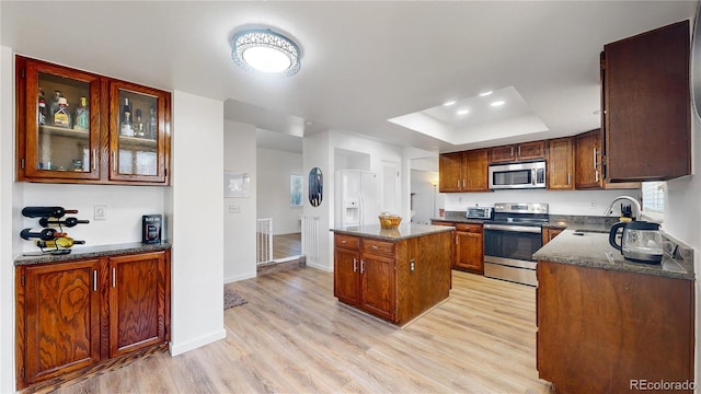 kitchen featuring dark stone counters, a raised ceiling, sink, appliances with stainless steel finishes, and a kitchen island