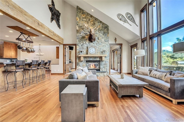 living room featuring a stone fireplace, a towering ceiling, a chandelier, and light hardwood / wood-style floors