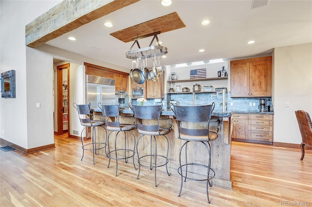 kitchen with a center island, a kitchen breakfast bar, light hardwood / wood-style flooring, built in appliances, and dark stone counters