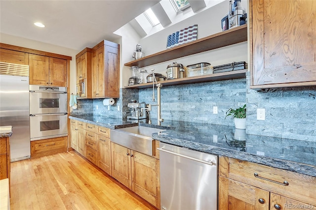 kitchen featuring light hardwood / wood-style flooring, a skylight, decorative backsplash, dark stone countertops, and appliances with stainless steel finishes