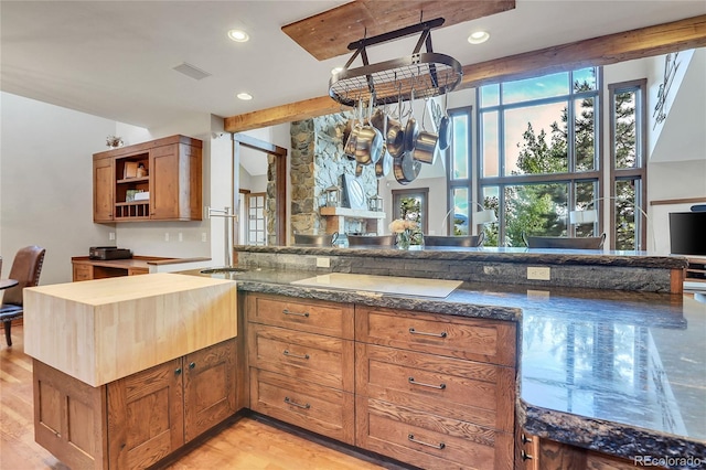 kitchen with beam ceiling, dark stone countertops, kitchen peninsula, and light hardwood / wood-style floors