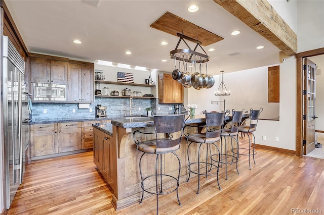 kitchen with a breakfast bar area, built in appliances, light hardwood / wood-style floors, and decorative light fixtures