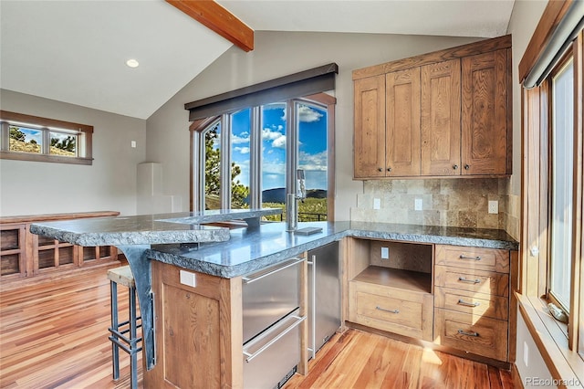 kitchen with vaulted ceiling with beams, backsplash, kitchen peninsula, light hardwood / wood-style floors, and a kitchen bar