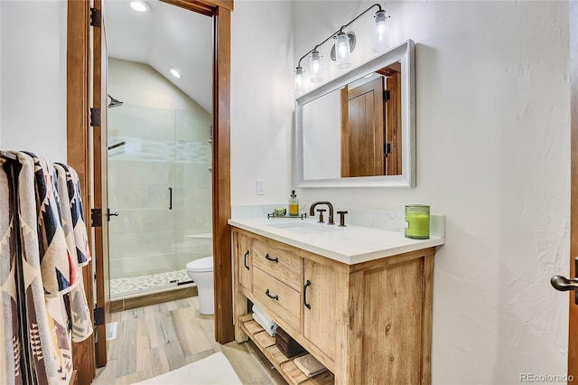 bathroom featuring a tile shower, hardwood / wood-style floors, vaulted ceiling, toilet, and vanity