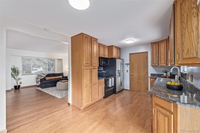 kitchen with light hardwood / wood-style floors, sink, black appliances, and dark stone counters