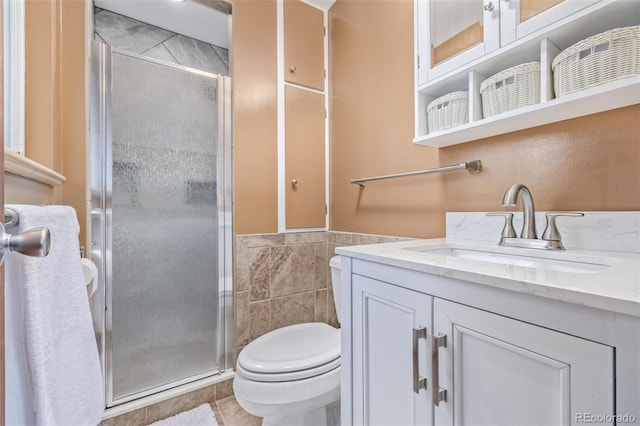 bathroom with a shower with door, tile walls, tile patterned flooring, vanity, and toilet