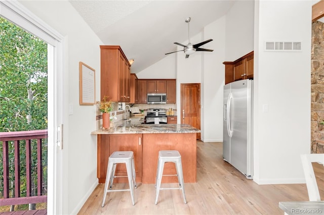 3260 Bit Rd, Evergreen, CO 80439 - kitchen with appliances with stainless steel finishes, a ceiling fan, a peninsula, light wood-style floors, and high vaulted ceiling