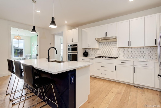 7029 Sagerock St, Castle Pines, CO 80108 - kitchen featuring a sink, appliances with stainless steel finishes, under cabinet range hood, tasteful backsplash, and white cabinetry