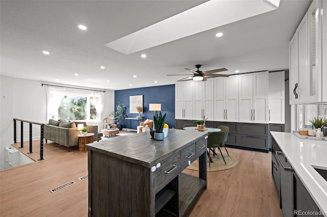 6742 Cole Cir, Arvada, CO 80004 - kitchen featuring light wood-style floors, a skylight, recessed lighting, white cabinetry, and open floor plan