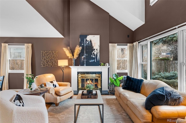 living room featuring high vaulted ceiling, a stone fireplace, and a wealth of natural light