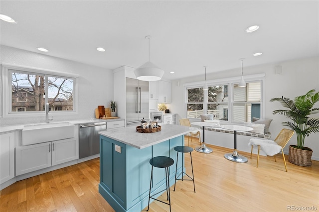 kitchen featuring a center island, sink, stainless steel dishwasher, pendant lighting, and white cabinets