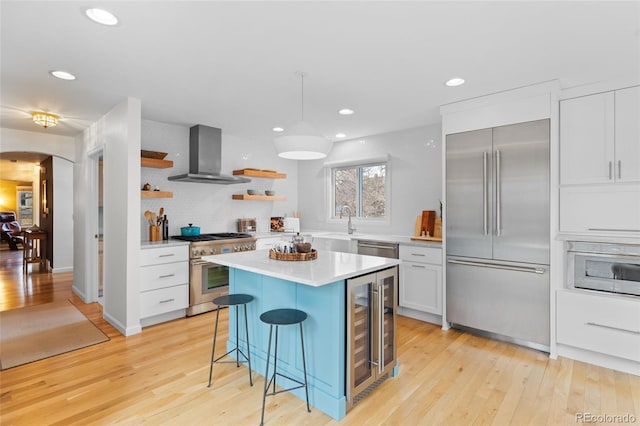 kitchen with wall chimney exhaust hood, a breakfast bar, high quality appliances, white cabinets, and a center island