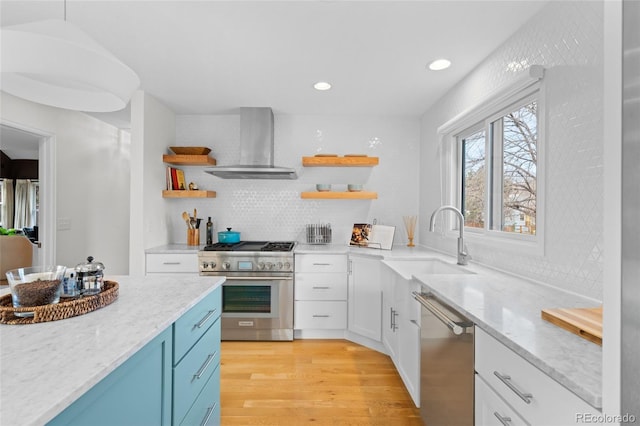 kitchen featuring white cabinets, wall chimney range hood, sink, light hardwood / wood-style floors, and stainless steel appliances