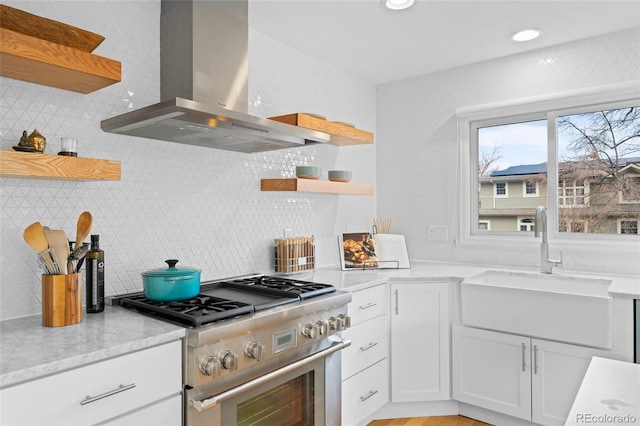 kitchen featuring backsplash, stainless steel range, sink, wall chimney range hood, and white cabinets