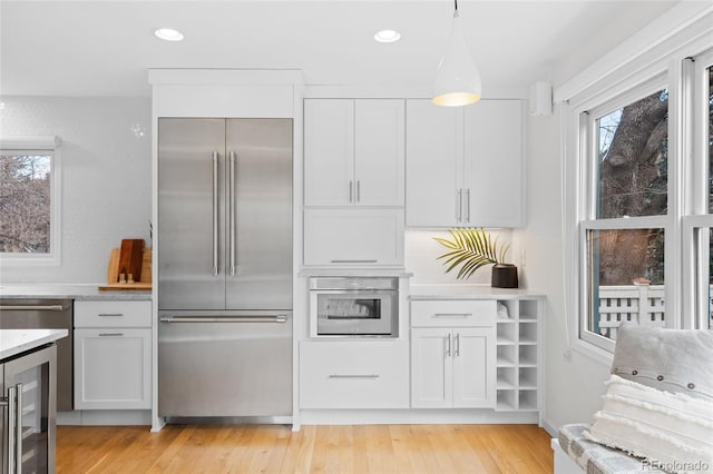 kitchen featuring appliances with stainless steel finishes, decorative light fixtures, light hardwood / wood-style flooring, white cabinets, and wine cooler