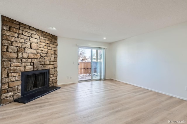 unfurnished living room featuring a textured ceiling, light hardwood / wood-style flooring, and a stone fireplace