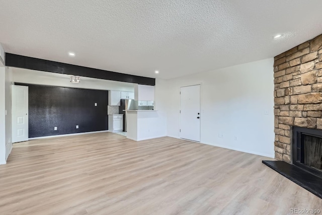 unfurnished living room with light wood-type flooring, a textured ceiling, a fireplace, and beamed ceiling